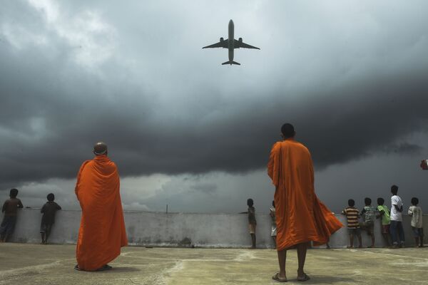Buddhists monks and children look out from the rooftop at a Buddhist mission hostel and school for underprivileged children as an international passenger flight takes off at the Netaji Subhash Chandra Bose International Airport after the authorities eased restrictions imposed as a preventive measure against the spread of  COVID-19, in Kolkata on 5 July 2020.  - Sputnik International