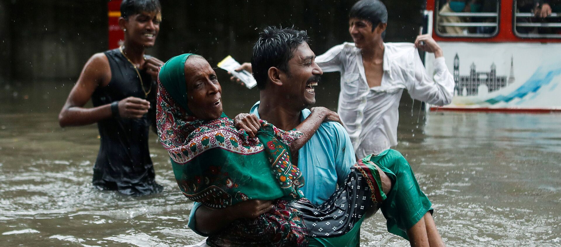 A man carries an elderly woman as they cross a waterlogged street during heavy rainfall in Mumbai, India, July 15, 2020 - Sputnik International, 1920, 16.07.2020