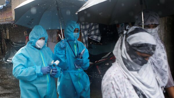 A health worker in personal protective equipment (PPE) walks holding an umbrella on a rainy day during a check up campaign for the coronavirus disease (COVID-19) in Mumbai, India, July 14, 2020 - Sputnik International