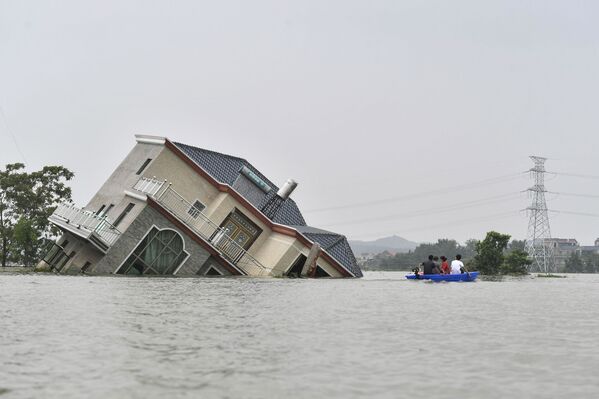 This photo taken on July 15, 2020 shows residents riding a boat past a damaged and flood-affected house near the Poyang Lake due to torrential rains in Poyang county, Shangrao city in China's central Jiangxi province - Sputnik International