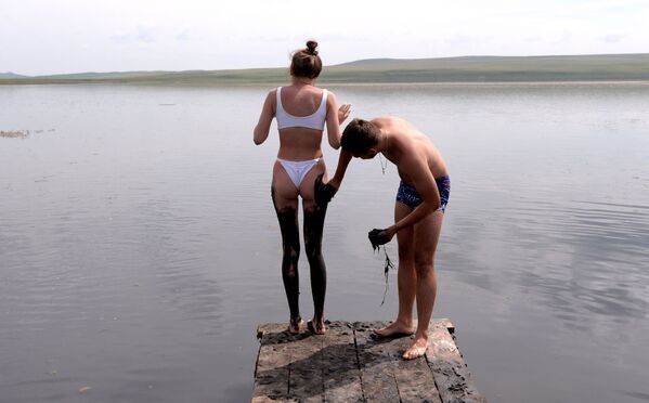 A man covers a girl with highly mineralised sulfide mud from the bottom sediments of the bitter-salt lake Tus in the Shirinsky district of the Republic of Khakassia, Russia - Sputnik International