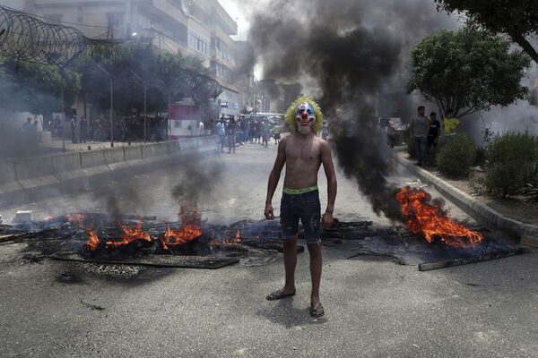 An anti-government demonstrator poses with a clown mask as others burn tires and wood to block a road in Beirut, Lebanon, Tuesday, July 14, 2020 - Sputnik International