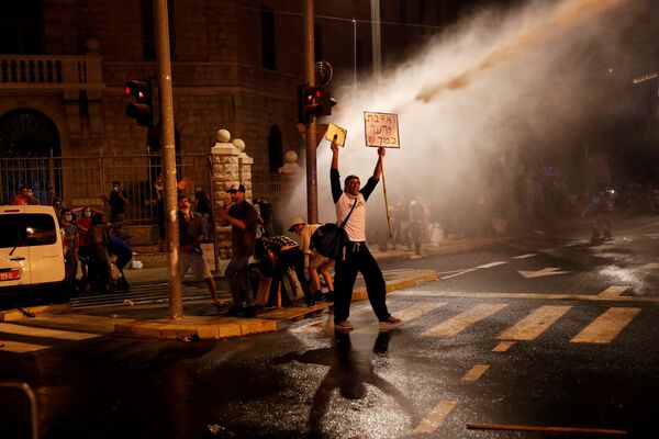 A protester stands as police use a water cannon during a protest against Israeli Prime Minister Benjamin Netanyahu and his government's response to the financial fallout of the coronavirus disease (COVID-19) crisis near Prime Minister Benjamin Netanyahu's residence in Jerusalem July 15, 2020 - Sputnik International