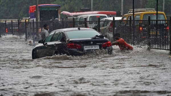 A man pushes a car, stuck in a flooded road, during heavy rains in Mumbai, India - Sputnik International