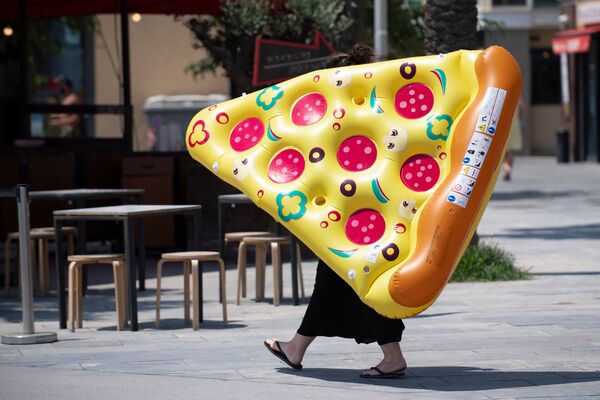 A woman carries an inflatable float with the shape of a portion of pizza in a Barcelona, on 18 July 2020
 - Sputnik International