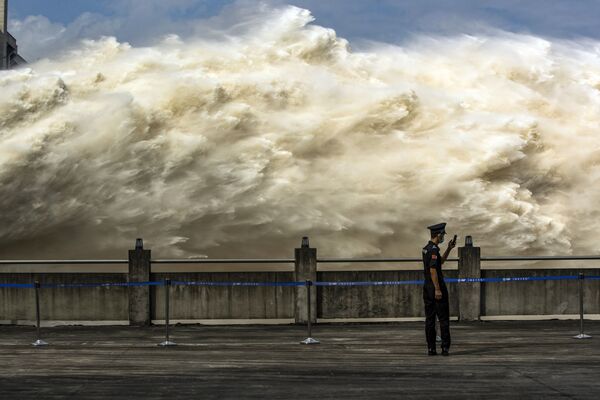 This photo taken on July 19, 2020, shows a security guard looking at his smartphone while water is released from the Three Gorges Dam, a gigantic hydropower project on the Yangtze river, to relieve flood pressure in Yichang, central China's Hubei province - Sputnik International