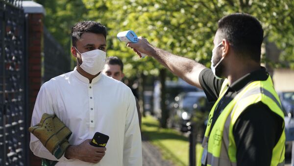 A man wearing a face mask has his temperature checked to try stop the spread of coronavirus, before being allowed to go into Manchester Central Mosque, in Manchester, northern England - Sputnik International