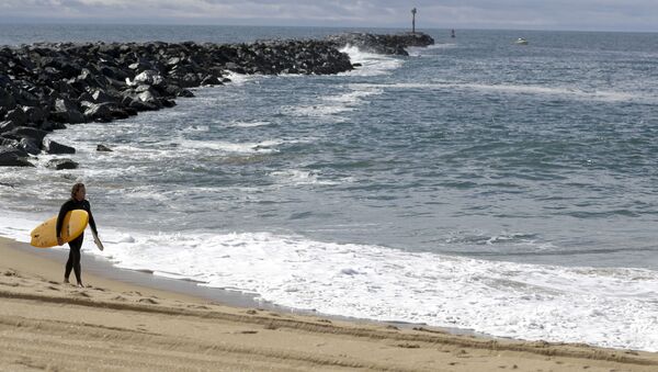 A lone surfer walks along a closed area of the beach in Newport Beach, Calif., Friday, 10 April 2020. The Wedge is closed to all surfboards and flotation devices from 10 a.m. to 5 p.m. May 1 through October 31 each year. - Sputnik International
