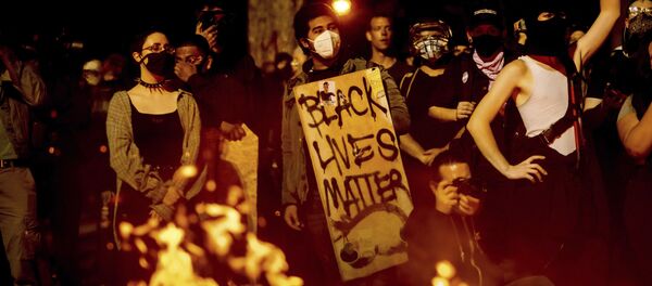 Black Lives Matter protester Jorge Mendoza holds a sign while rallying at the Mark O. Hatfield United States Courthouse on Saturday, Aug. 1, 2020, in Portland, Ore. Following an agreement between Democratic Gov. Kate Brown and the Trump administration to reduce federal officers in the city, nightly protests remained largely peaceful without major confrontations between demonstrators and officers. Black Lives Matter protester Jorge Mendoza holds a sign while rallying at the Mark O. Hatfield United States Courthouse on Saturday, Aug. 1, 2020, in Portland, Ore. Following an agreement between Democratic Gov. Kate Brown and the Trump administration to reduce federal officers in the city, nightly protests remained largely peaceful without major confrontations between demonstrators and officers. - Sputnik International
