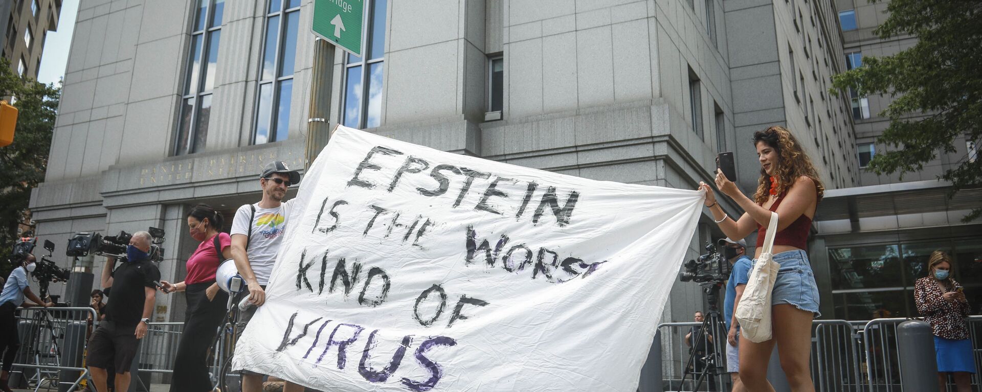 Multimedia artist Katelyn Kopenhaver, right, with help from her brother Brent Kopenhaver, unfurls a banner reading [Jefferey] Epstein is the worst kind of virus, outside federal court where a judge held a bail hearing by video for Epstein's former girlfriend Ghislaine Maxwell, Tuesday, July 14, 2020, in New York. - Sputnik International, 1920, 04.01.2024