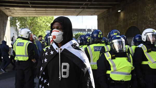 A member of Black Lives Matter movement, draped on a black and white U.S. flag, stands in front of British police officers in riot gear following a protest in central London, Saturday, June 13, 2020. - Sputnik International
