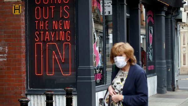 A woman wearing a protective face mask walks past a sign in Manchester - Sputnik International