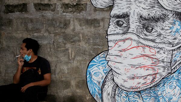 A man smokes a cigarette next to a mural of a man wearing a protective mask amid the coronavirus disease (COVID-19) outbreak in Quezon City, Metro Manila, Philippines, July 30, 2020.  - Sputnik International