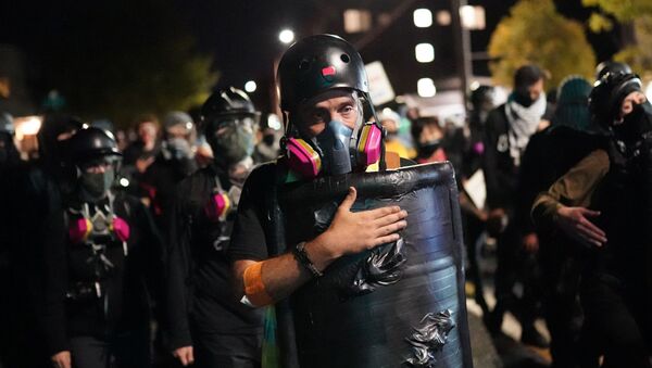 A protesters slaps his shield while marching toward the Portland Police Bureau North Precinct on the 75th day of protests against racial injustice and police brutality on August 10, 2020 in Portland, Oregon. Crowd sizes began growing again last week as protesters regularly march on city and county law enforcement buildings. - Sputnik International