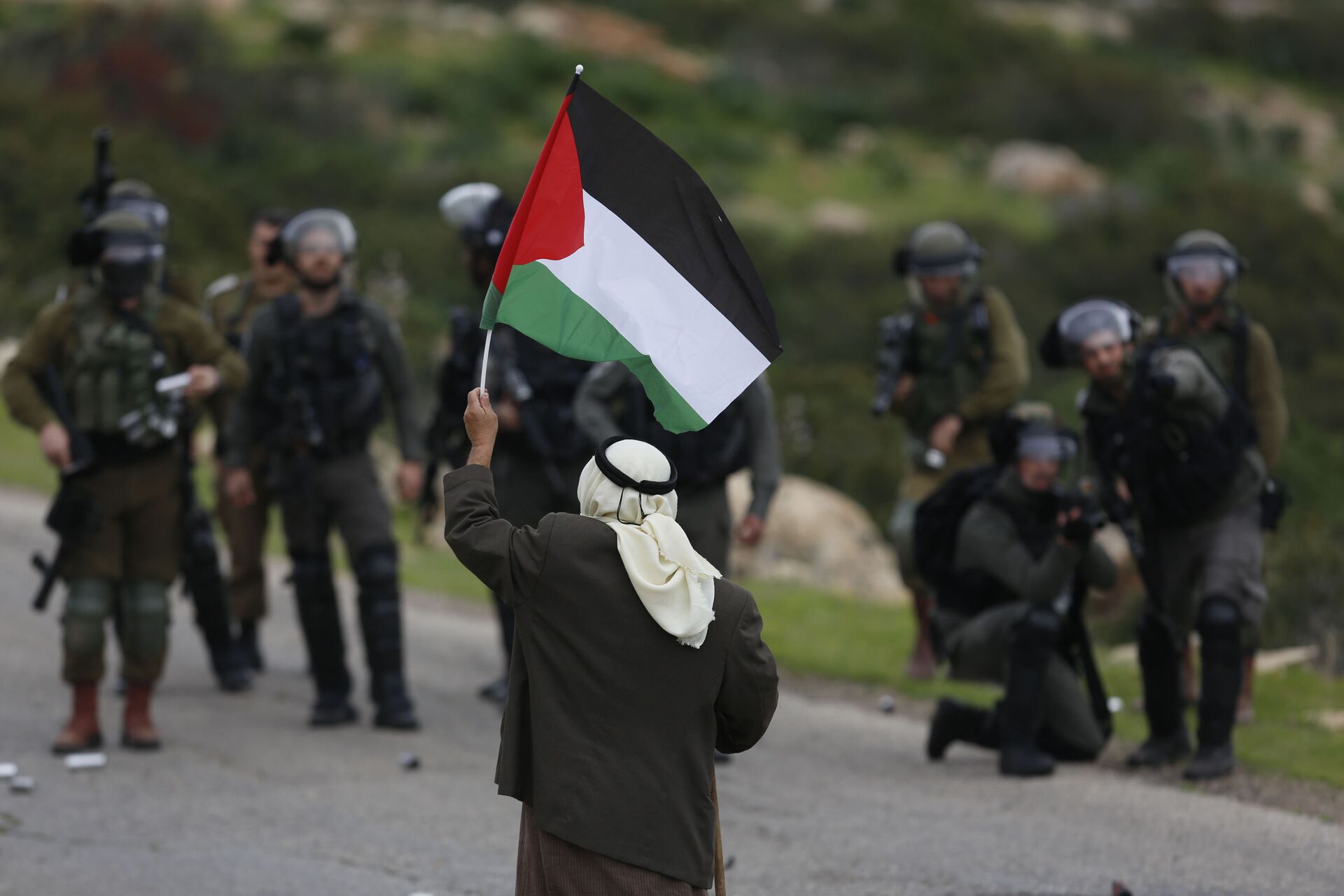 A Palestinian demonstrator holds a national flags in front of Israeli forces as they protest against President Donald Trump's Mideast initiative, in Jordan Valley in the West Bank, Tuesday, Feb. 25, 2020 - Sputnik International, 1920, 19.07.2022