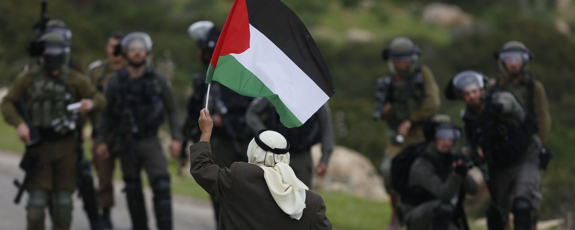 A Palestinian demonstrator holds a national flags in front of Israeli forces as they protest against President Donald Trump's Mideast initiative, in Jordan Valley in the West Bank, Tuesday, Feb. 25, 2020 - Sputnik International, 1920, 22.05.2024