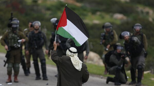 A Palestinian demonstrator holds a national flags in front of Israeli forces as they protest against President Donald Trump's Mideast initiative, in Jordan Valley in the West Bank, Tuesday, Feb. 25, 2020 - Sputnik International