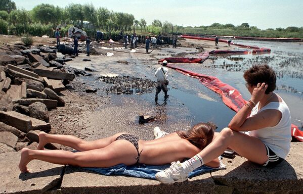Sunbathers watch workers clean up oil spilled on the resort beach of Playa Nueva in Magdalena, Argentina, 100 km (62 miles) south of Buenos Aires, 21 January 1999. - Sputnik International