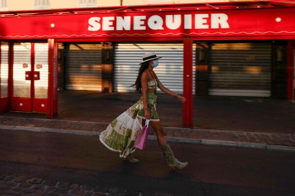 A woman wearing a face mask walks past the closed Le Cafe Senequier situated along the Quai Jean Jaures, on the Saint-Tropez harbour on 16 August 2020, as the city made wearing a protective mask mandatory in the town centre due to a resurgence of the coronavirus.   - Sputnik International