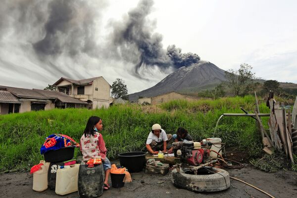 Villagers do their laundry as Mount Sinabung spews volcanic materials during an eruption, in Karo, North Sumatra, Indonesia Friday, 14 August 2020.  - Sputnik International