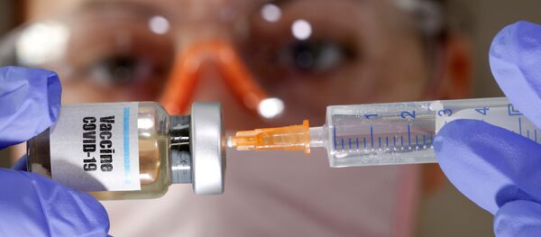A woman holds a small bottle labeled with a Vaccine COVID-19 sticker and a medical syringe in this illustration taken April 10, 2020. - Sputnik International