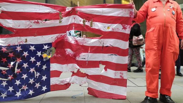 Tattered US flag upside-down with protester in orange jumpsuit holding placard with Hands Off Assange message - Sputnik International