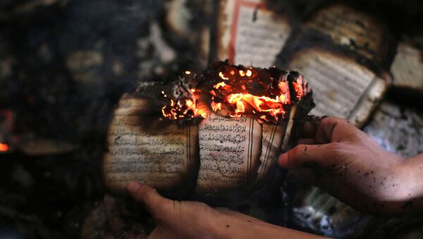 A Palestinian man displays a copy of Islam's holy book, the Koran, still burning inside a mosque that was set ablaze by Israeli settlers in al-Mughayir, in the occupied West Bank near the Jewish settlement of Shilo, on November 12, 2014. - Sputnik International