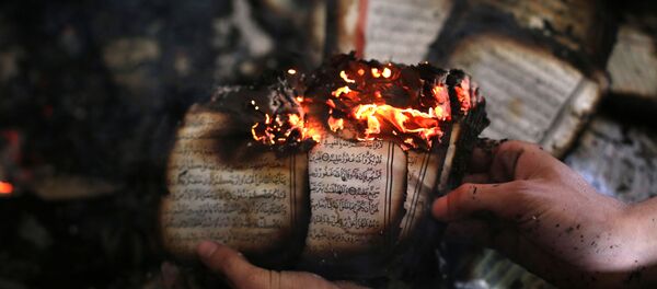A Palestinian man displays a copy of Islam's holy book, the Koran, still burning inside a mosque that was set ablaze by Israeli settlers in al-Mughayir, in the occupied West Bank near the Jewish settlement of Shilo, on November 12, 2014. A Palestinian man displays a copy of Islam's holy book, the Koran, still burning inside a mosque that was set ablaze by Israeli settlers in al-Mughayir, in the occupied West Bank near the Jewish settlement of Shilo, on November 12, 2014. - Sputnik International