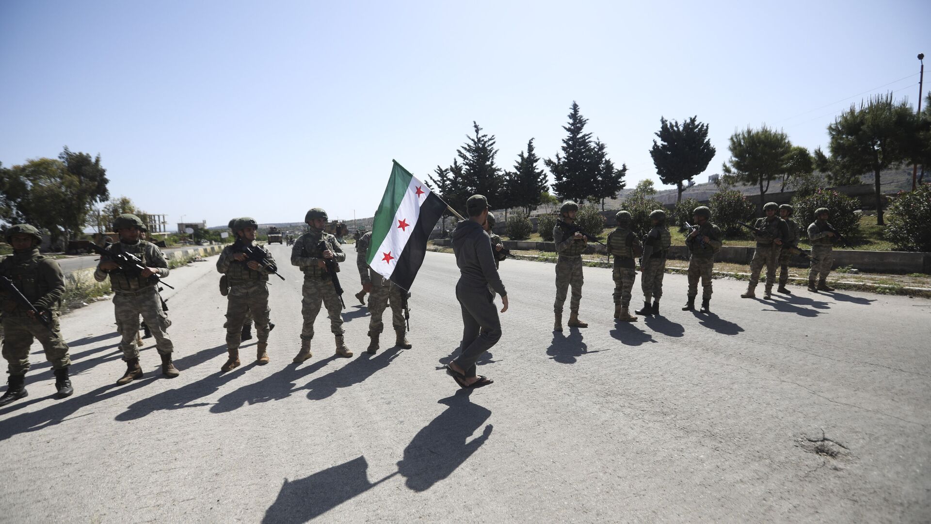 A man carries Syrian Independence flag as Turkish soldiers block a road after a nearby explosion outside the city of Ariha, in Idlib province, Syria, Tuesday, May 12, 2020 - Sputnik International, 1920, 30.10.2021
