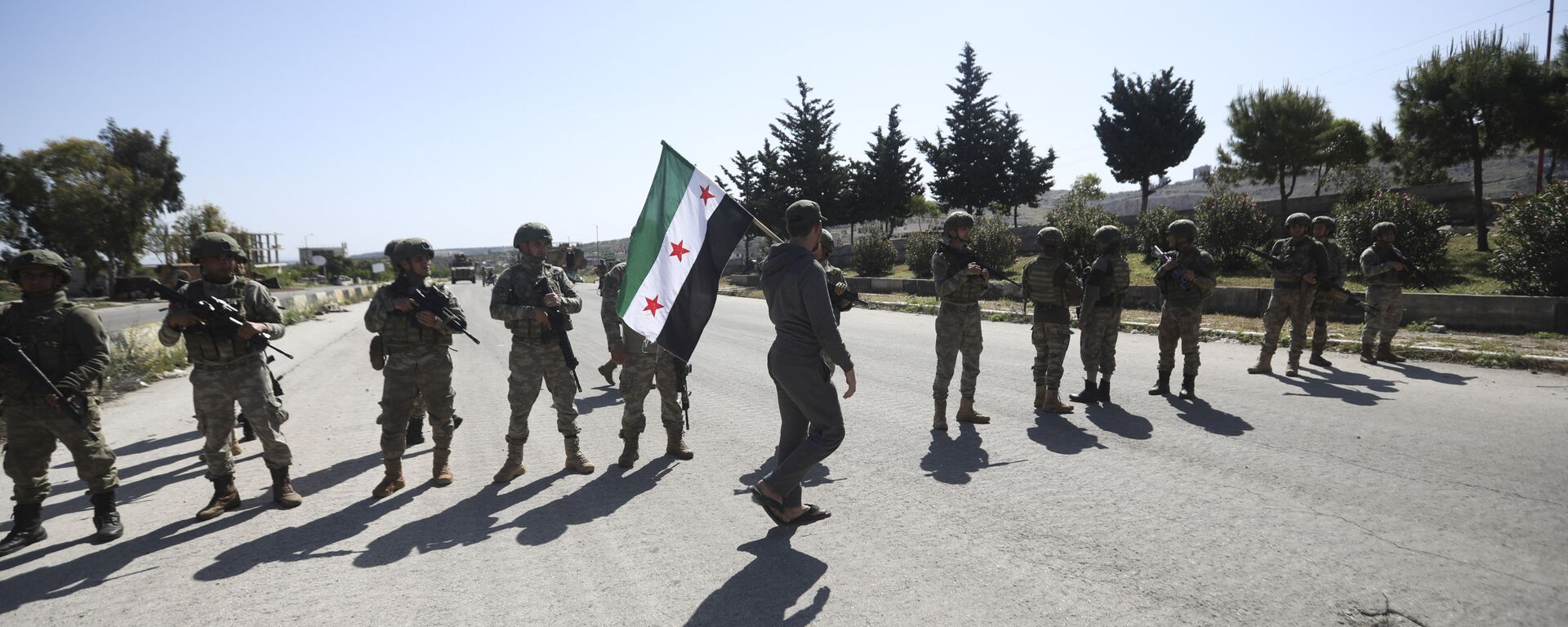 A man carries Syrian Independence flag as Turkish soldiers block a road after a nearby explosion outside the city of Ariha, in Idlib province, Syria, Tuesday, May 12, 2020 - Sputnik International, 1920, 30.10.2021