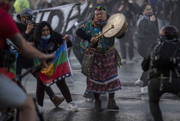 A Mapuche indigenous woman plays the drum as riot police use water cannons to disperse demonstrators during a protest against the government's handling of the COVID-19 novel coronavirus pandemic, in Santiago, on September 4, 2020 - Sputnik International