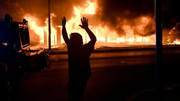 A man walks by an armoured vehicle as B&L Office Furniture burns in the background as protests turn to fires after a Black man, identified as Jacob Blake, was shot several times by police last night in Kenosha, Wisconsin, U.S. August 24, 2020. Picture taken August 24, 2020.  - Sputnik International