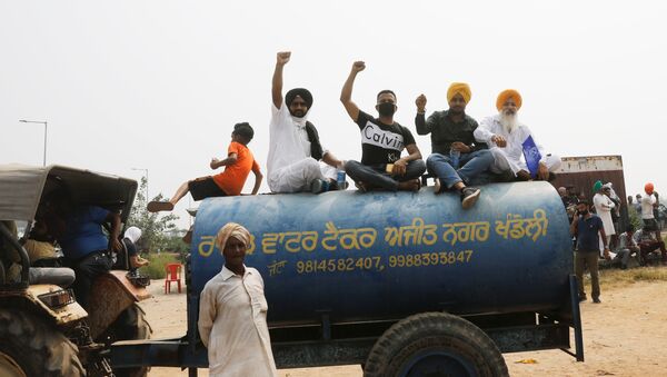 Farmers sit on the water tank as they block a national highway during a protest against farm bills passed by India's parliament - Sputnik International