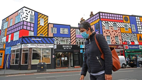 A woman wearing a face mask walks past shops and a mural created by artist Camille Walala, amid the spread of the coronavirus disease (COVID-19), in Leyton, London, Britain, September 29, 2020 - Sputnik International