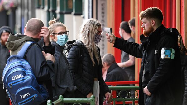 A security guard uses a handheld thermometer to take the temperature of customers, wearing face masks or coverings due to the COVID-19 pandemic, as they wait to enter a bar in Liverpool, north west England on October 2, 2020, following the  announcement of new local restrictions for certain areas in the northwest of the country, due to a resurgence of novel coronavirus cases. - The British government on Thursday extended lockdowns to Liverpool and several other towns in northern England, effectively putting more than a quarter of the country under tighter coronavirus restrictions. Health Secretary Matt Hancock said limits on social gatherings would be extended to the Liverpool City region, which has a population of about 1.5 million. (Photo by Oli SCARFF / AFP) - Sputnik International