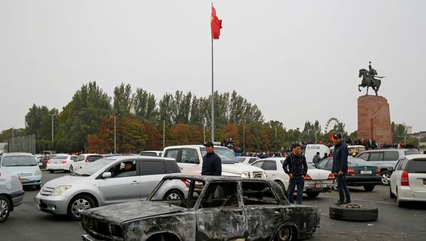 People stand next to a car burnt during a protest against the results of a parliamentary election in Bishkek, Kyrgyzstan, October 6, 2020. - Sputnik International
