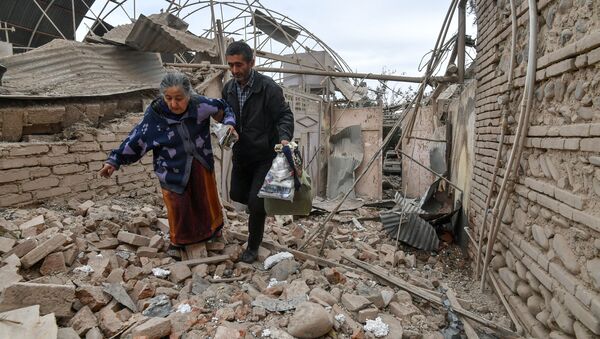 A man helps an elderly woman to walk out of a damaged house carrying her belongings following the recent shelling by Armenian forces, in Ganja, Azerbaijan.  - Sputnik International