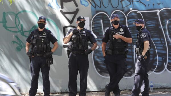 Seattle Police officers stand in front of a wall of graffiti as they wait across the street from a rally in support of police and other law enforcement officers, Wednesday, July 15, 2020, in front of City Hall in Seattle - Sputnik International