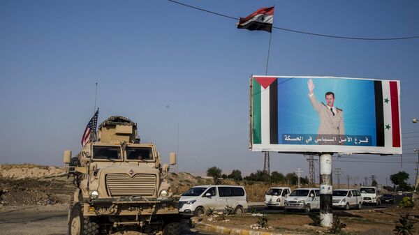 FILE - In this Saturday, 26 October 2019 file photo, a US military vehicle drives south of the northeastern city of Qamishli, likely heading to the oil-rich Deir el-Zour area where there are oil fields, or possibly to another base nearby, as it passes by a poster showing Syrian President Bashar Assad. - Sputnik International