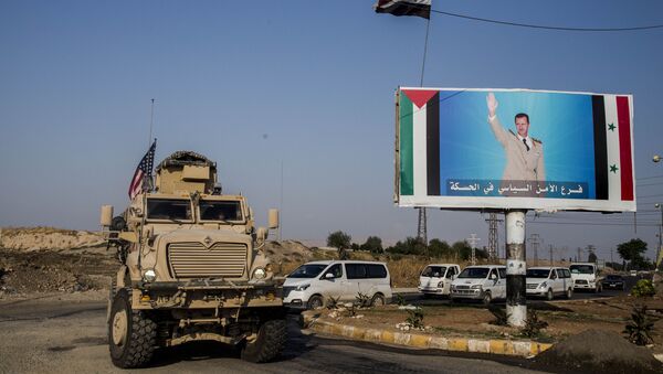 FILE - In this Saturday, 26 October 2019 file photo, a US military vehicle drives south of the northeastern city of Qamishli, likely heading to the oil-rich Deir el-Zour area where there are oil fields, or possibly to another base nearby, as it passes by a poster showing Syrian President Bashar Assad. - Sputnik International