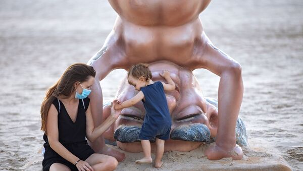 A woman wearing a protective face mask plays with her daughter next to a statue of the first Israeli Prime Minister David Ben Gurion, during a nationwide three-week lockdown to curb the spread of the coronavirus at the beach in Tel Aviv, Israel, Tuesday, Sept 22, 2020. - Sputnik International