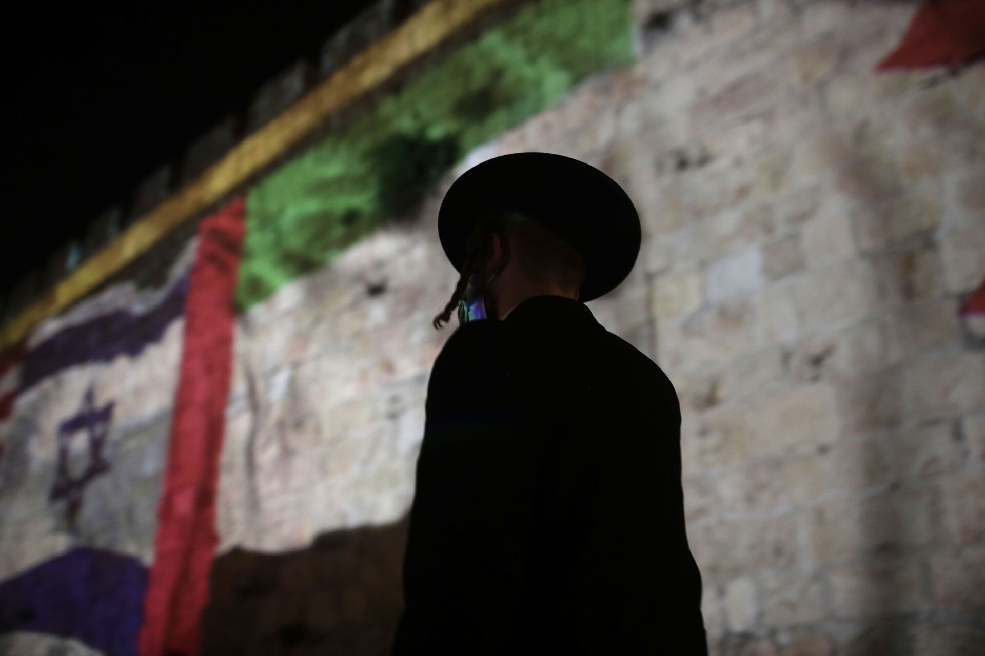 An ultra-Orthodox Jewish man walks past representations of the Israeli, Emirati and Bahraini flags projected onto a wall of Jerusalem's Old City, marking the day of a signing ceremony in Washington signifying the two Gulf nations' normalization of relations with Israel, Tuesday, Sept. 15, 2020.  - Sputnik International, 1920, 02.11.2021