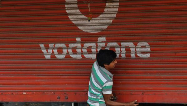 A staff opens the shutter of a shop depicting an advertisement of the telecom company Vodafone in Mumbai on February 21, 2020 - Sputnik International