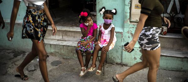 Девочки в масках ждут своих родителей, сидя на стуле в Гаване, Куба - Sputnik International