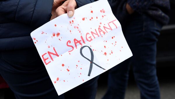 A person holds a placard reading 'Bleeding (a French play on words with the word Teachers and the French word for 'Bleeding)' near the entrance of a middle school in Conflans-Sainte-Honorine, 30kms northwest of Paris, on October 17, 2020, after a teacher was decapitated by an attacker who has been shot dead by policemen. - The man suspected of beheading on October 16 ,2020 a French teacher who had shown his students cartoons of the prophet Mohammed was an 18-year-old born in Moscow and originating from Russia's southern region of Chechnya, a judicial source said on October 17. Five more people have been detained over the murder on October 16 ,2020 outside Paris, including the parents of a child at the school where the teacher was working, bringing to nine the total number currently under arrest, said the source, who asked not to be named. The attack happened at around 5 pm (1500 GMT) near a school in Conflans-Sainte-Honorine, a western suburb of the French capital. The man who was decapitated was a history teacher who had recently shown caricatures of the Prophet Mohammed in class. - Sputnik International