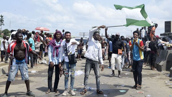 A protester waves a Nigerian national flag behind barricades mounted on the Lagos-Ibadan expressway to protest against police brutality and the killing of protesters by the military, at Magboro, Ogun State, on October 21, 2020 - Sputnik International