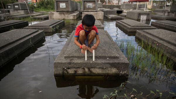 A boy attempts to keep a candle lit in a flooded cemetery following Typhoon Molave, in Masantol, Pampanga, Philippines, October 27, 2020 - Sputnik International