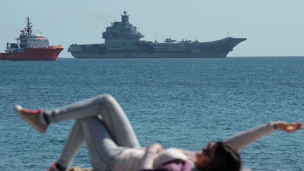 A woman enjoy the sea and the sun as in the background see the Russian aircraft carrier Admiral Kuznetsov lies at anchor off Cyprus’ largest port of Limassol on Thursday, Feb. 27, 2014 - Sputnik International