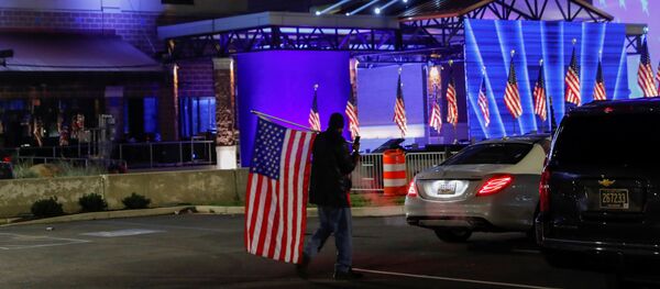 A Biden supporter carries an American flag across the parking lot where U.S. Democratic presidential nominee Joe Biden will hold his 2020 U.S. presidential election night event as a drive-in rally because of coronavirus disease (COVID-19) pandemic social distancing, in Wilmington, Delaware, U.S., November 3, 2020.   - Sputnik International