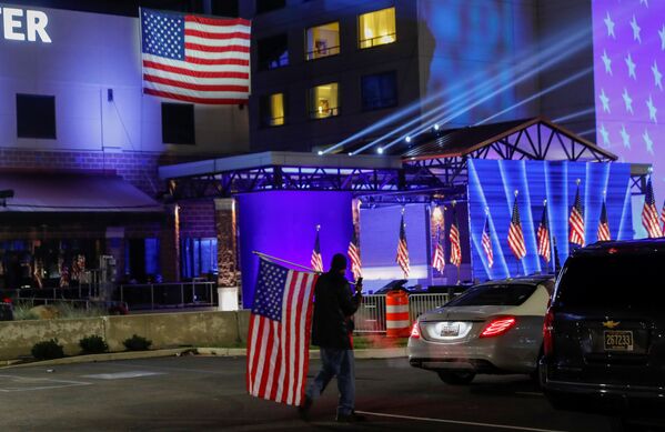 A Biden supporter carries an American flag across the parking lot where US presidential nominee for the Democrats, Joe Biden, will hold his 2020 US presidential election night event as a drive-in rally because of coronavirus restrictions, in Wilmington, Delaware, US, 3 November 2020.   - Sputnik International